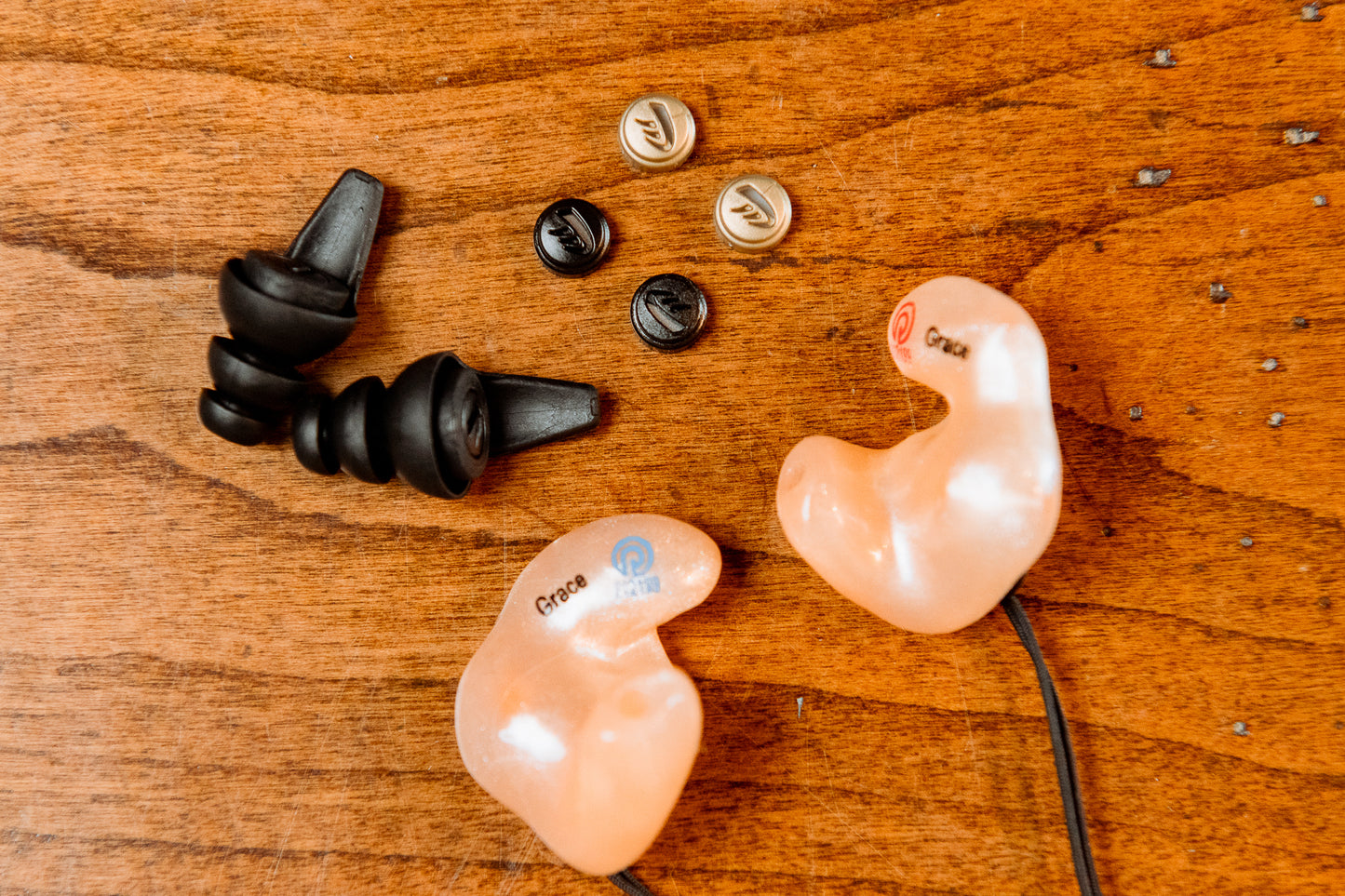 OtoPro custom-fit sleeve earpieces with OtoPro Impulse filters displayed on wooden surface — personalized earmolds for upgraded hearing protection