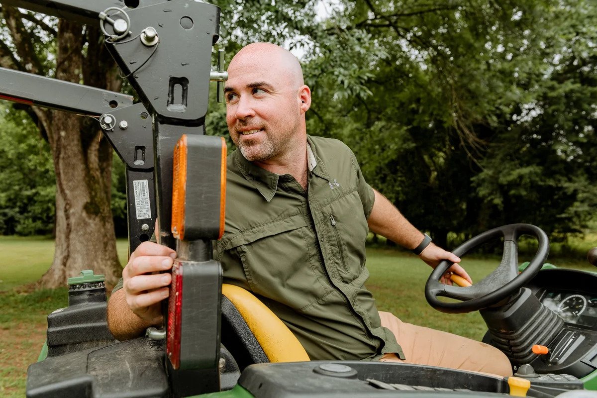 Man operating farm tractor wearing OtoPro Impulse earplugs — hearing protection for landscaping and construction